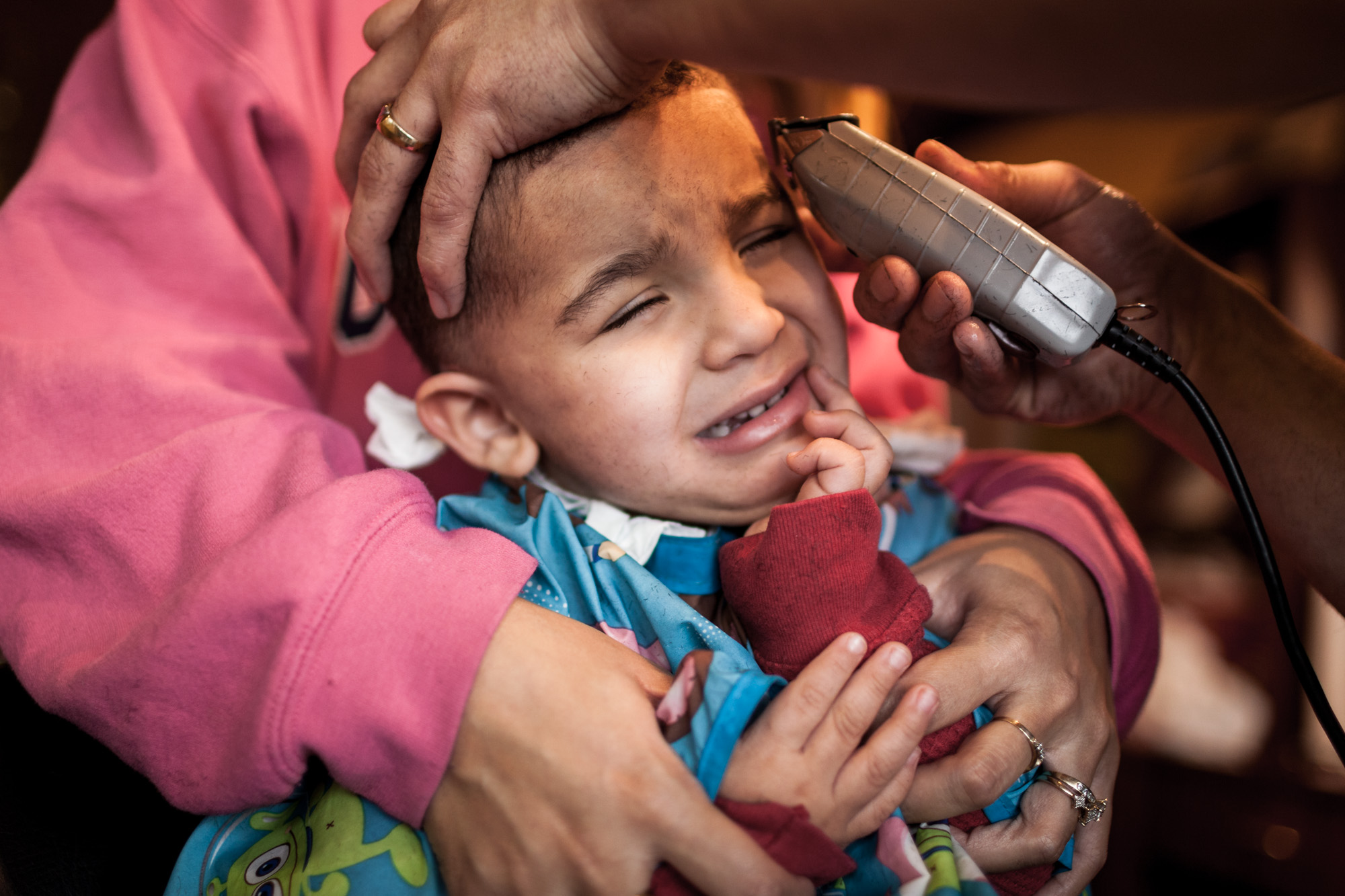  2 year old David Quick is held down by his mother Vanessa Quick as Junior, a barber at Top Notch Barbering salon in Rochester's Swillburg neighborhood gives him his first haircut, Friday, January 25, 2013.