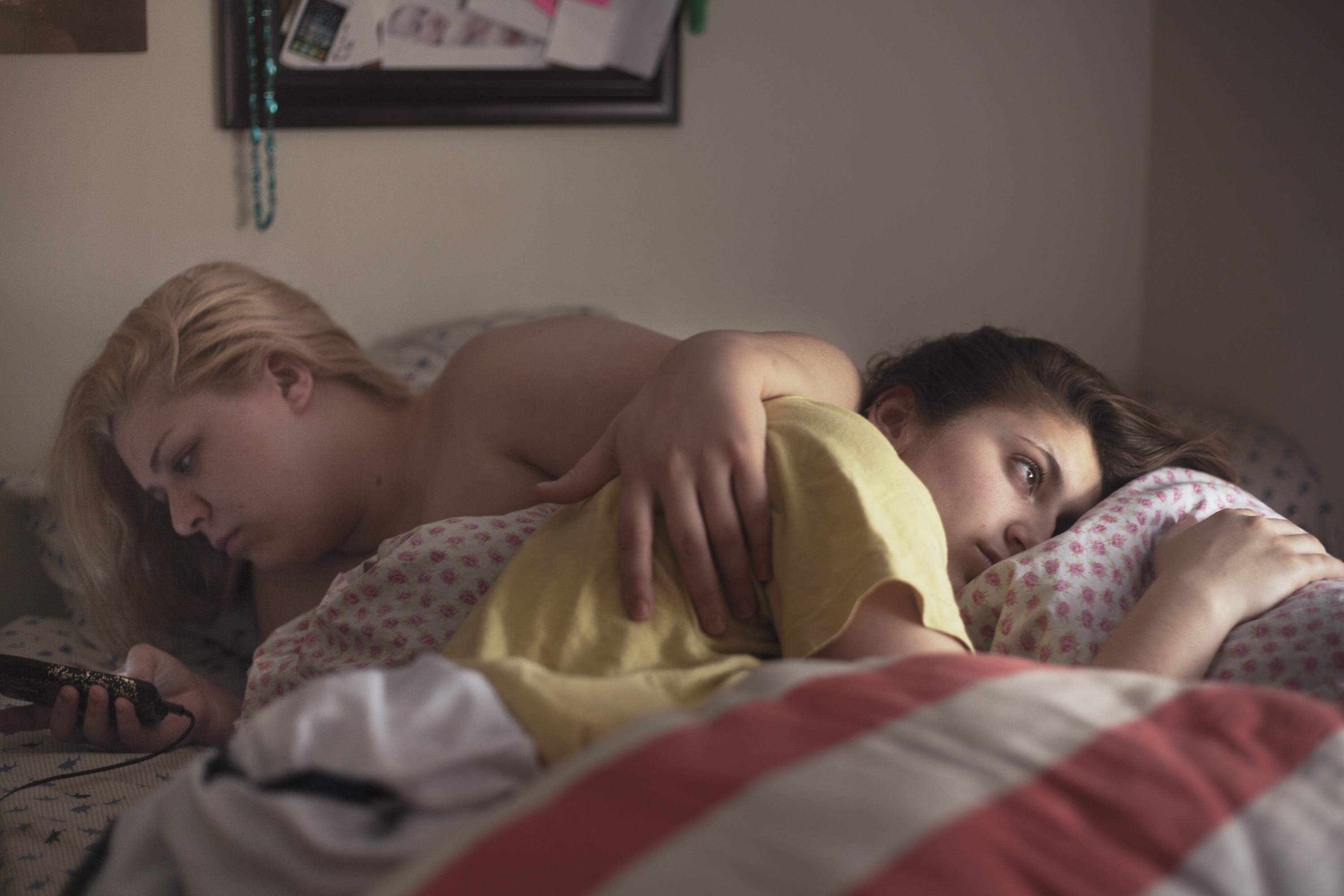 Hannah Kanik, 20, checks her phone while her girlfriend, Courtney DiStasio, 20, looks out the window when they wake up in the morning. Courtney and Hannah’s relationship have been both affirming to one another, but Hannah’s turbulent lifestyle leaves Courtney drained sometimes. Photo by Evan Ortiz