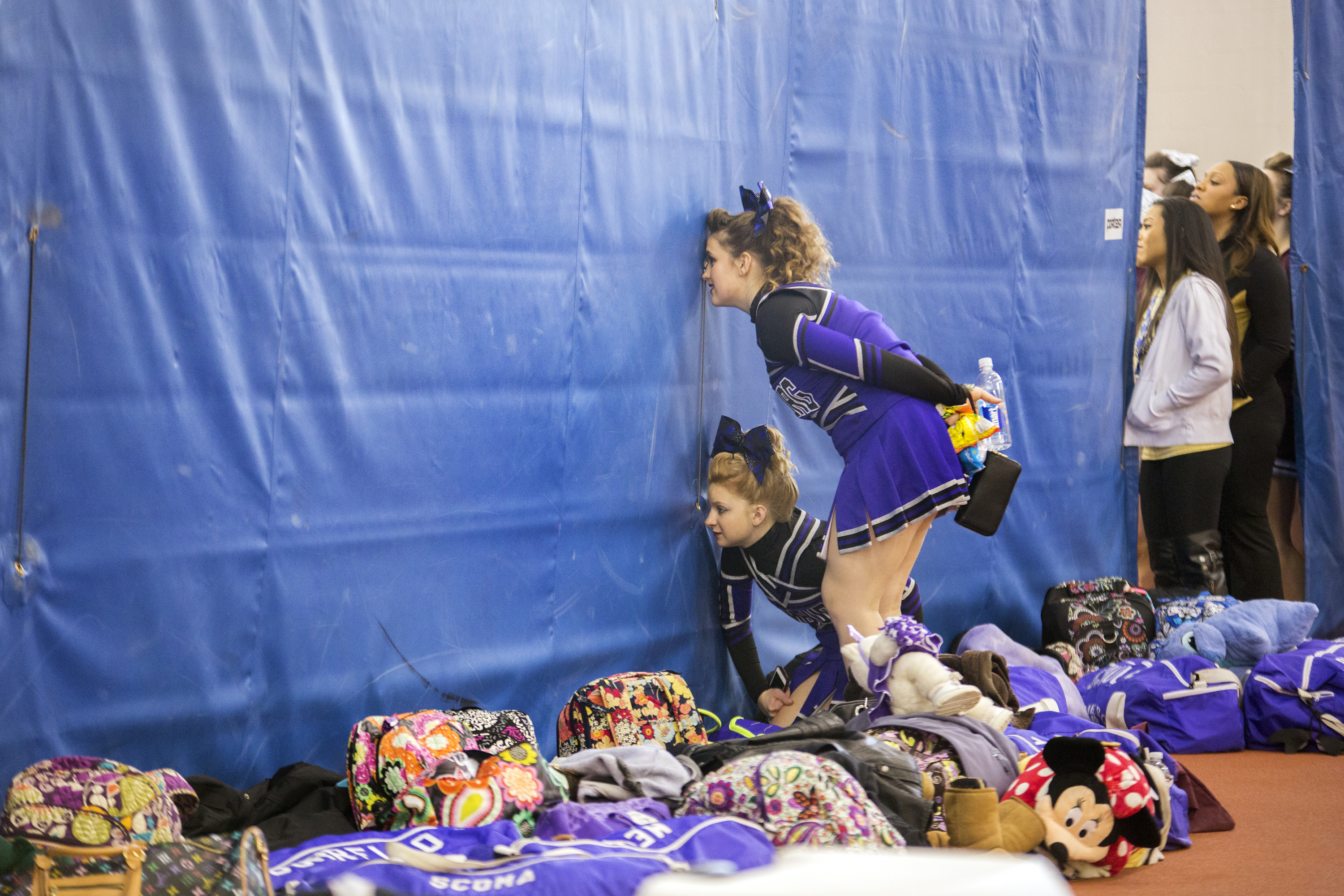 Hamburg Varsity competitive cheer teammates Maya Fagnan, below, and Ava O'Hara, above look through curtain holes at another team's performance during the  NYSPHAA State Cheerleading qualifiers cheer competition on March 7, 2015 in Henrietta, N.Y.