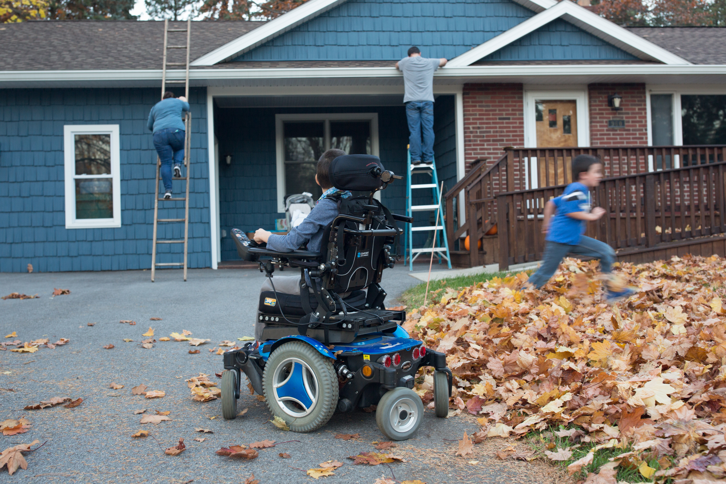 Josh Nodine, 8, watches as his parents setup christmas lights and Caleb Nodine, 6, runs into a leaf pile on Friday, November 18, 2016. Josh was diagnosed with Cerebral Palsy as an infant.
