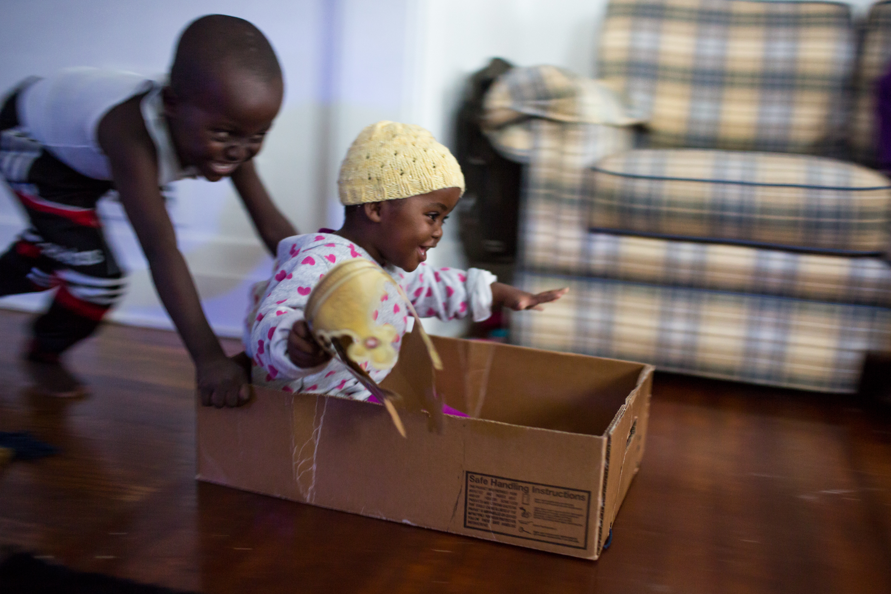 Hassan Abdikadir, 5, pushes his sister, Khadijo, 2, across the living room floor in a cardboard box, as she holds a paper crown from their first ever visit to a Burger King earlier in the day, on Dec. 9, 2016, in the family's newly settled apartment in Rochester, N.Y. The Abdikadir family moved to Rochester in November of 2016 from a refugee camp in Kenya, after leaving their native home of Somalia nearly ten years prior.